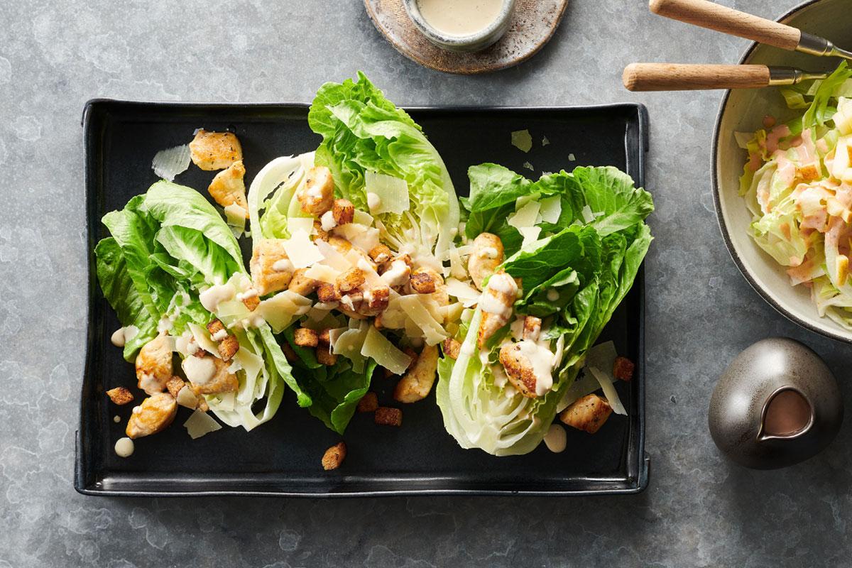 Blick auf eine dunkle, rechteckige Form, in der Salat mit Croutons und hellen Fleischstückchen angerichtet ist